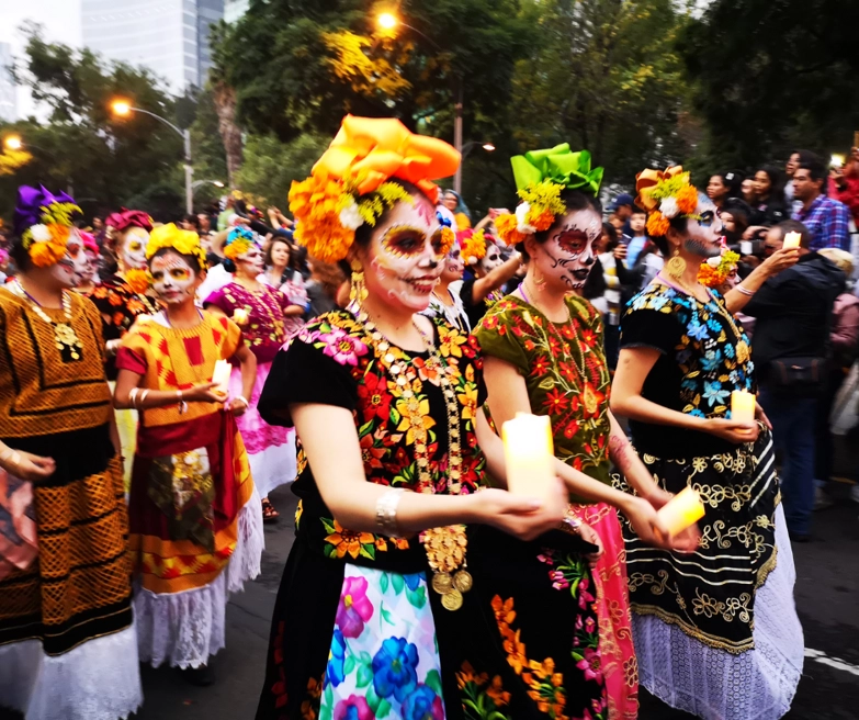 A group of women walking down a street in a performance as part of a Hispanic Culture Festival. Attendees are watching on the side.