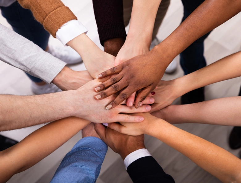 A group of people of different races placing their hands together in a circle.